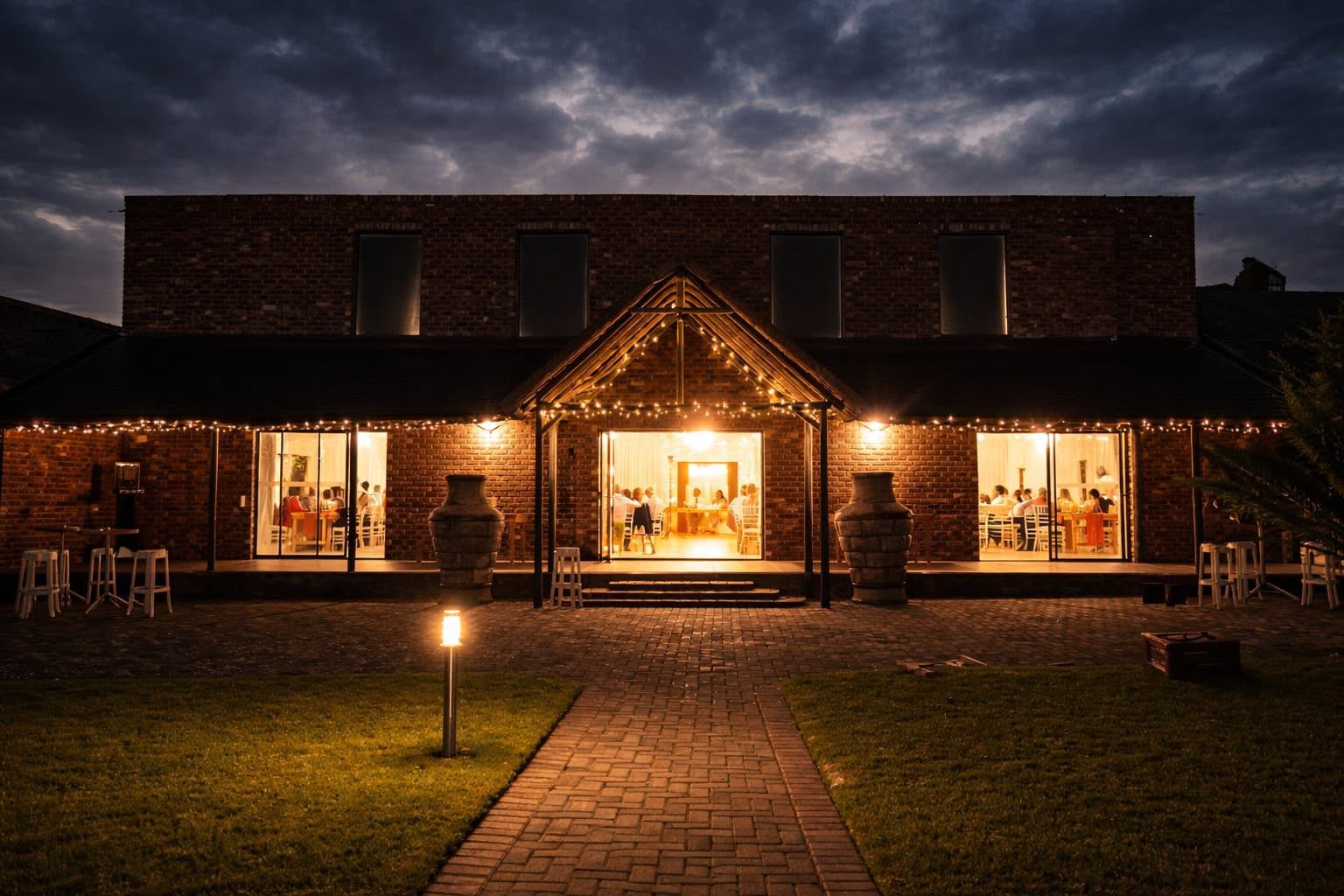 The Ukuphupha Main Hall at night, its doors open and glowing with fairy lights